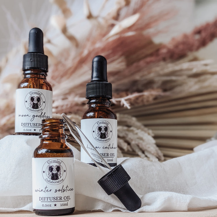 Photo of three half ounce glass bottles of diffuser oils with glass pipettes arranged in front of dried florals
