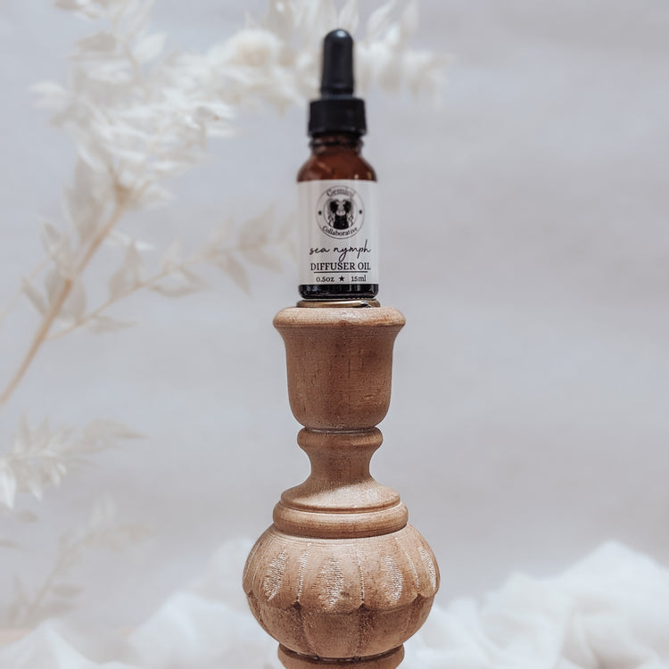 Photo of diffuser oil in half ounce glass bottle with glass pipette ion a wood pedestal with florals in the background