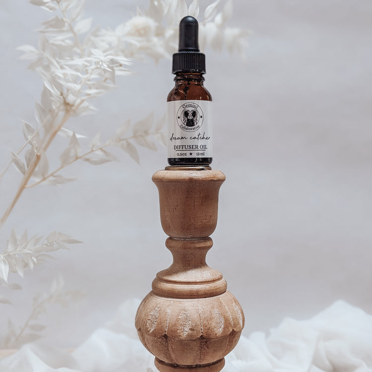 Photo of diffuser oil in half ounce glass bottle with glass pipette ion a wood pedestal with florals in the background