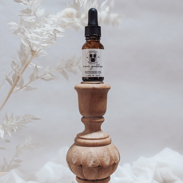 Photo of diffuser oil in half ounce glass bottle with glass pipette ion a wood pedestal with florals in the background