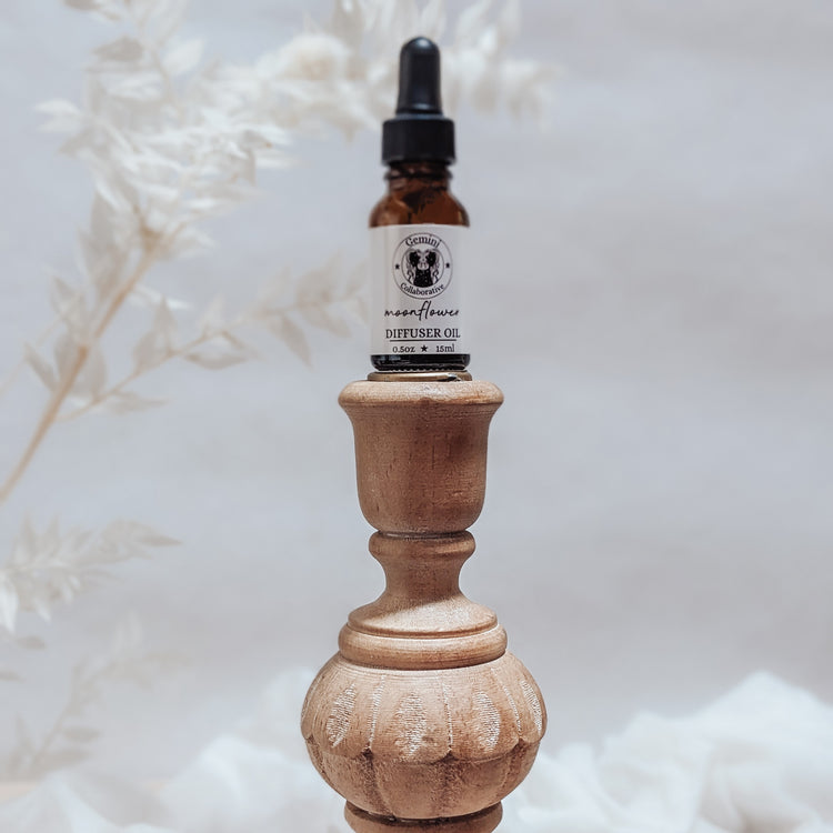 Photo of diffuser oil in half ounce glass bottle with glass pipette ion a wood pedestal with florals in the background