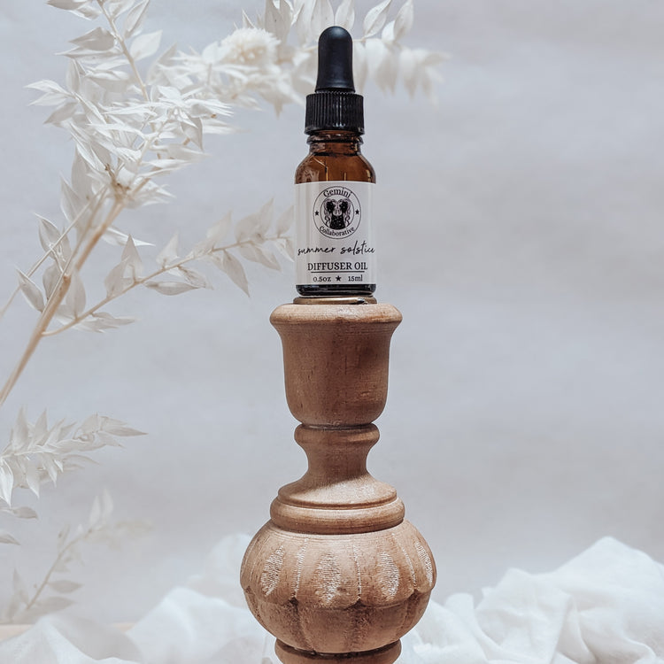 Photo of diffuser oil in half ounce glass bottle with glass pipette ion a wood pedestal with florals in the background