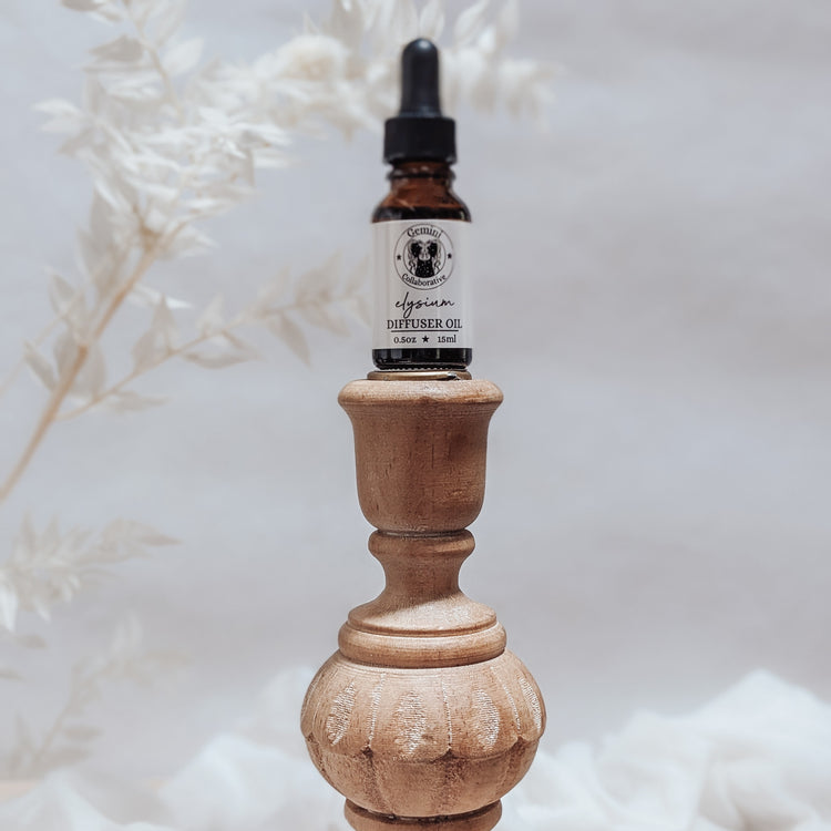 Photo of diffuser oil in half ounce glass bottle with glass pipette ion a wood pedestal with florals in the background
