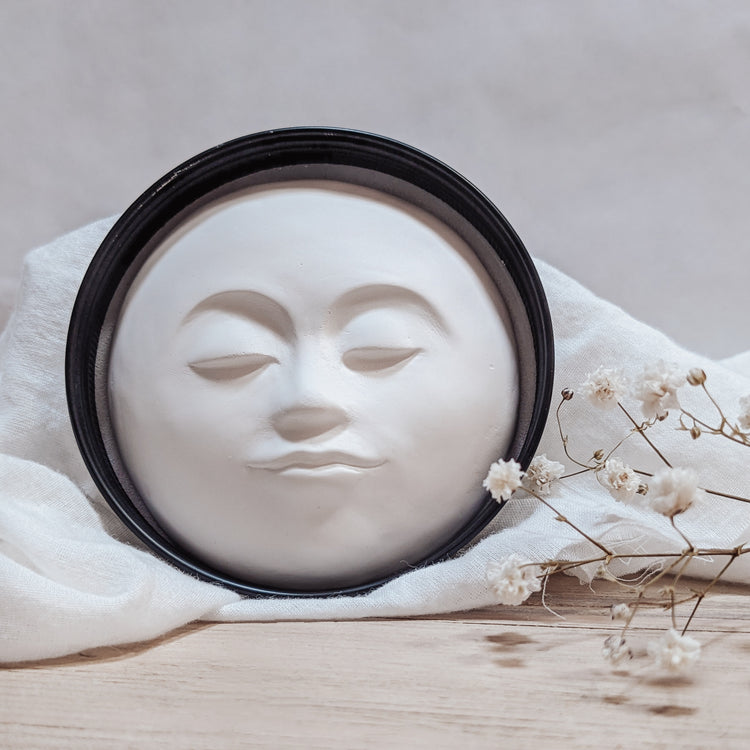 Photo of a lid to a small tin with a plaster aroma stone with a molded face and florals in the background.