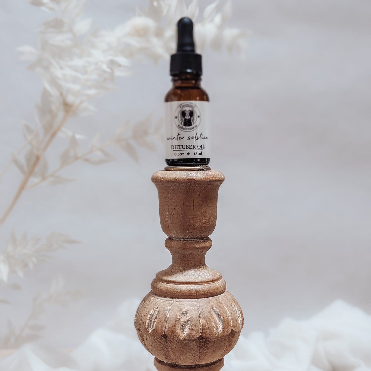 Photo of diffuser oil in half ounce glass bottle with glass pipette ion a wood pedestal with florals in the background