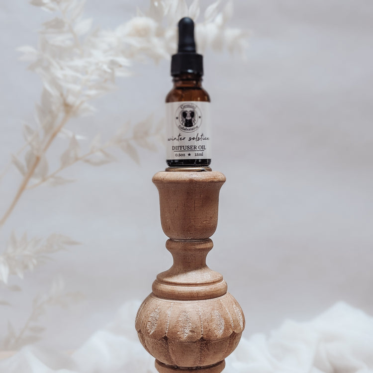 Photo of diffuser oil in half ounce glass bottle with glass pipette ion a wood pedestal with florals in the background