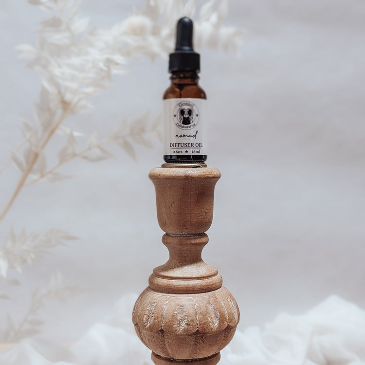 Photo of diffuser oil in half ounce glass bottle with glass pipette ion a wood pedestal with florals in the background