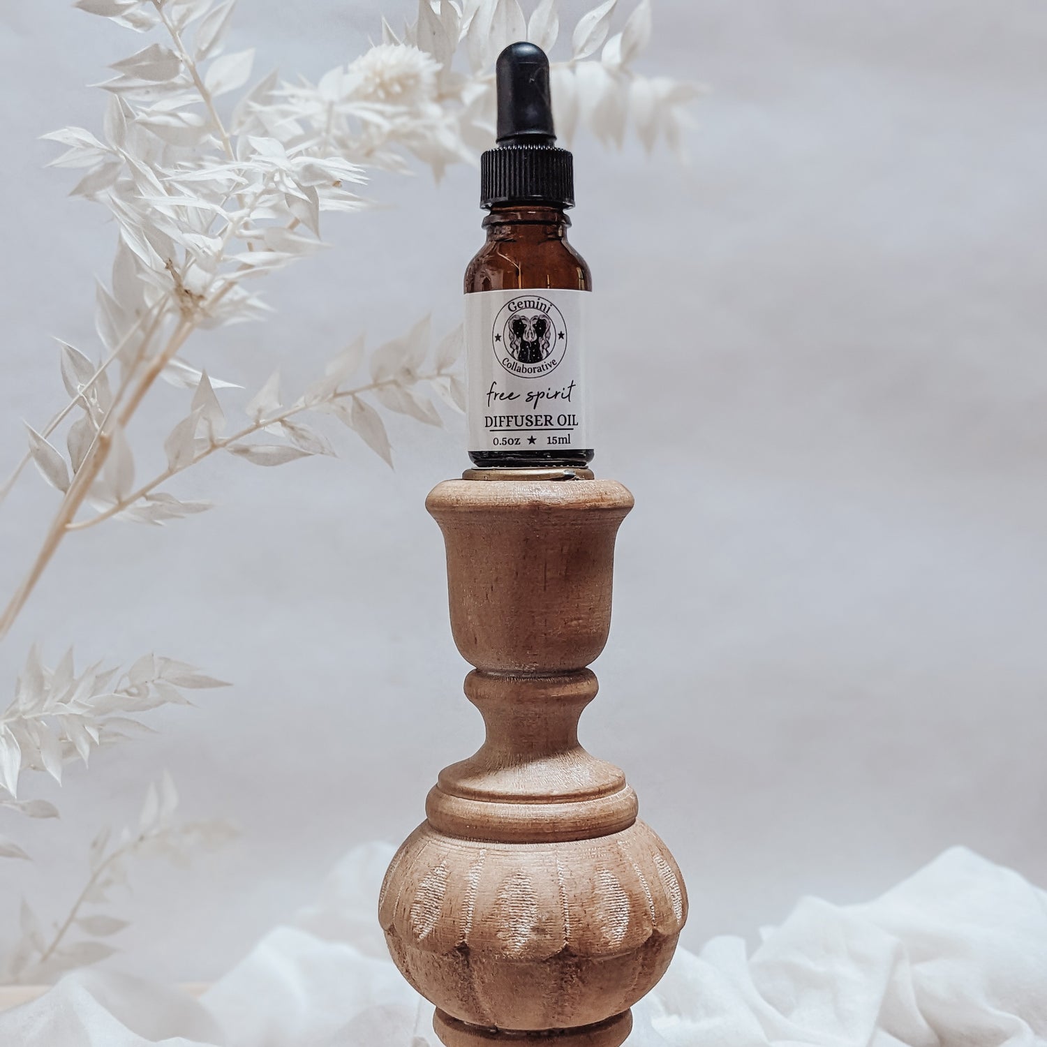 Photo of diffuser oil in half ounce glass bottle with glass pipette ion a wood pedestal with florals in the background