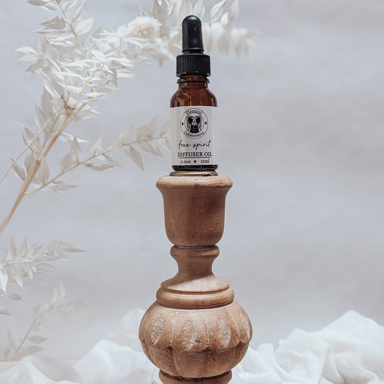 Photo of diffuser oil in half ounce glass bottle with glass pipette ion a wood pedestal with florals in the background