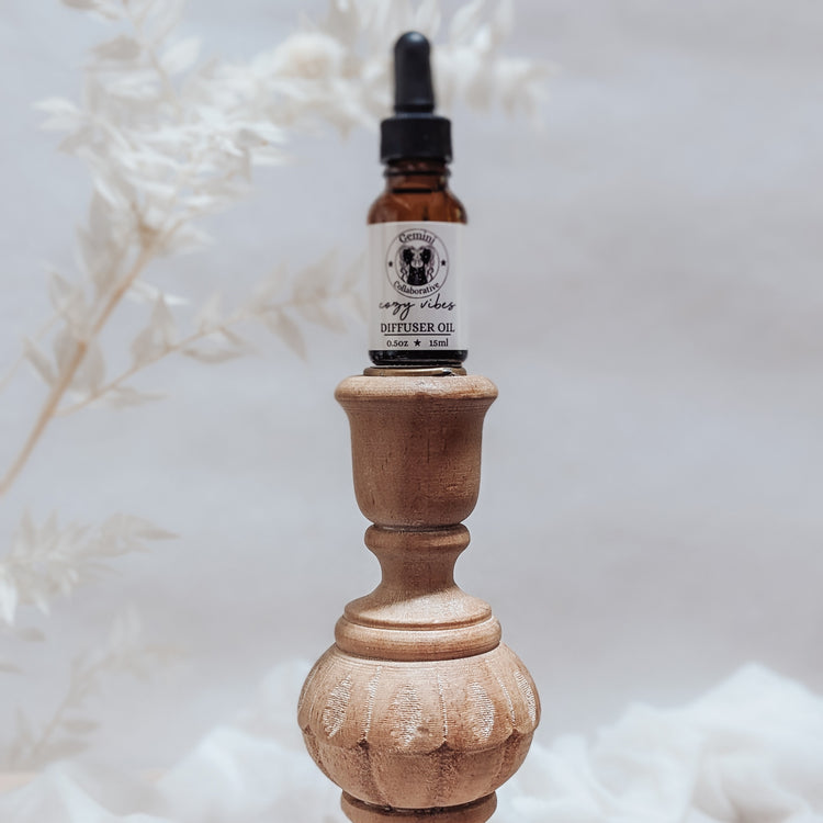 Photo of diffuser oil in half ounce glass bottle with glass pipette ion a wood pedestal with florals in the background